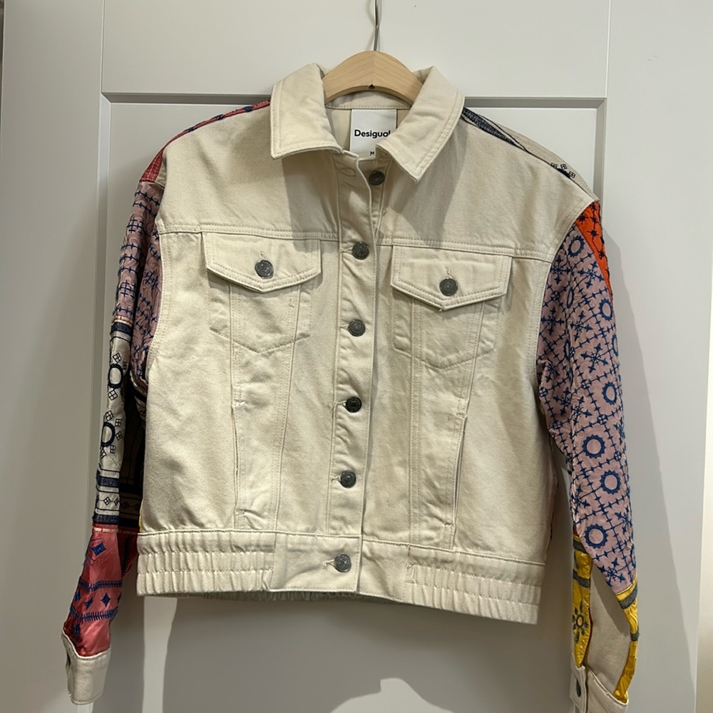 A short denim trucker-style jacket with a patchwork of embroidery
